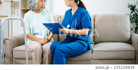 Asian nurse examines knee and leg pain of an elderly woman on a sofa at home, focusing on joint pain, arthritis and modern home healthcare care. Asian nurse examines knee and leg pain of an elderly woman on a sofa at home, focusing on joint pain, arthritis and modern home healthcare care. 135226939