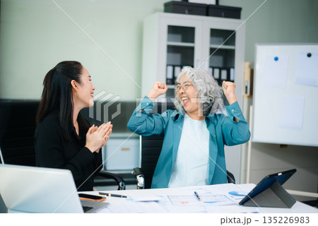 Asian senior and middle aged businesswomen reviewing documents and reports in office. Professional teamwork, mentorship, business collaboration 135226983