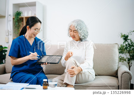 Asian Nurse Using Tablet to Review Bone X-ray Results with Elderly Woman at Home, Home Healthcare Concept Asian Nurse Using Tablet to Review Bone X-ray Results with Elderly Woman at Home, Home Healthcare Concept 135226998