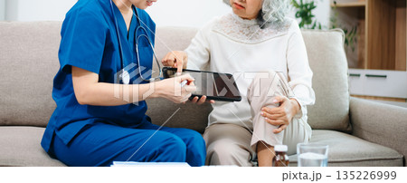 Asian Nurse Using Tablet to Review Bone X-ray Results with Elderly Woman at Home, Home Healthcare Concept Asian Nurse Using Tablet to Review Bone X-ray Results with Elderly Woman at Home, Home Healthcare Concept 135226999