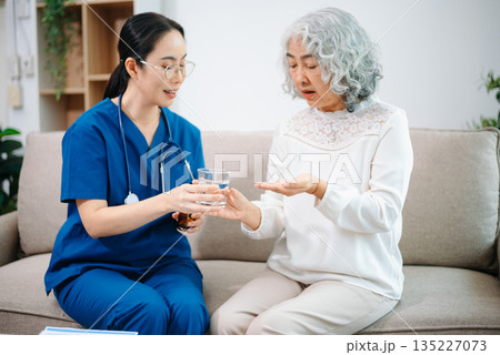 Young nurse holding a bottle of pills and discussing treatment with an elderly Asian woman during a medical consultation Young nurse holding a bottle of pills and discussing treatment with an elderly Asian woman during a medical consultation 135227073