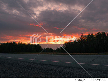 Sunset over a rural road surrounded by trees at dusk creating a serene atmosphere Sunset over a rural road surrounded by trees at dusk creating a serene atmosphere 135229385
