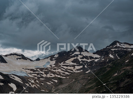 Mountain range partially covered by clouds and snow near a glacier on an overcast day in Caucasus Mountain range partially covered by clouds and snow near a glacier on an overcast day in Caucasus 135229386