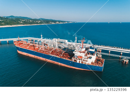 Aerial view of a large oil tanker docked at a pier in the port in process of loading. 135229396