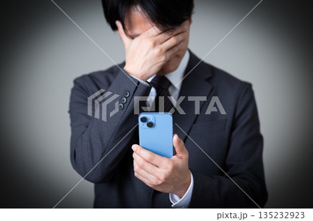 スマホを見て落ち込むスーツ姿のミドル男性ビジネスマン スマホを見て落ち込むスーツ姿のミドル男性ビジネスマン 135232923
