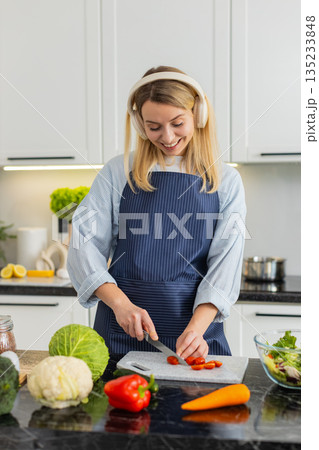 Young woman chopping tomatoes for keto salad while listening to music for meal prep in home kitchen Young woman chopping tomatoes for keto salad while listening to music for meal prep in home kitchen 135233848