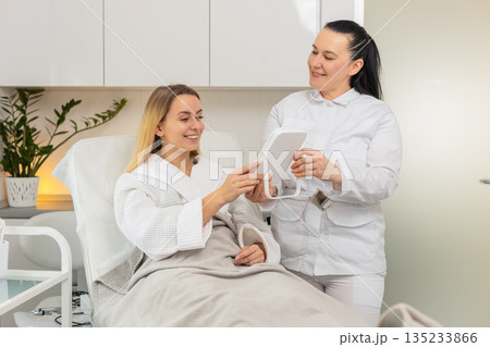Middle-aged woman smiling in mirror after cosmetic procedure in clinic with visible skin results 135233866
