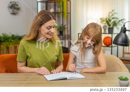 Mother daughter play tic tac toe on paper rounds keep score notebook laugh rematch at table together 135233897