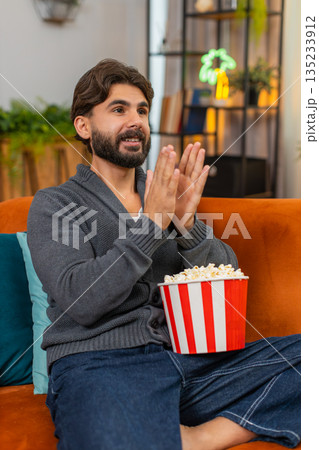 Indian man watches series finale on laptop with popcorn tense pause then claps hands happy reaction Indian man watches series finale on laptop with popcorn tense pause then claps hands happy reaction 135233912