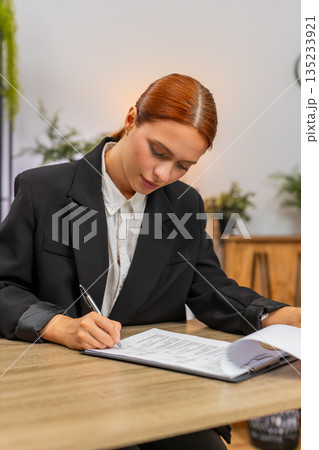 Young businesswoman carefully signs contract turning pages and securing important business agreement Young businesswoman carefully signs contract turning pages and securing important business agreement 135233921