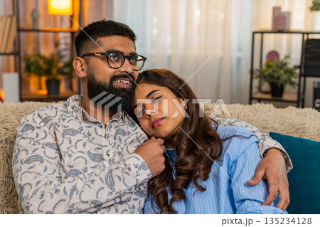 Indian couple man woman sleeping at home, girl resting on shoulder while boy touches hair gently 135234128