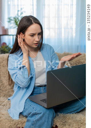 Young woman irritated sits on sofa arguing over laptop poor video call emotionally gesturing angry Young woman irritated sits on sofa arguing over laptop poor video call emotionally gesturing angry 135234149