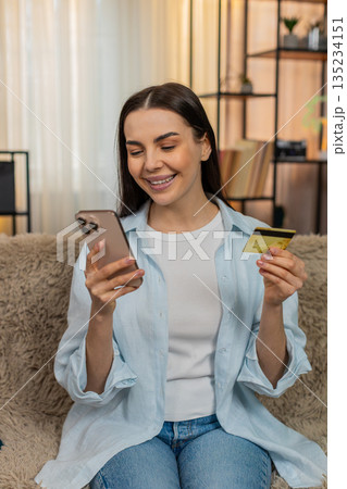 Young woman on sofa carefully entering credit card details on smartphone making online payment Young woman on sofa carefully entering credit card details on smartphone making online payment 135234151