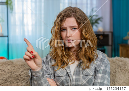 Woman sitting on sofa waving hand no with serious face expression showing disagreement and refusal 135234157