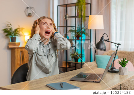 Frustrated freelancer using laptop struggling to work due to loud noise sitting at home office table Frustrated freelancer using laptop struggling to work due to loud noise sitting at home office table 135234188