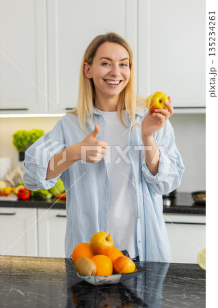 Young woman eating fresh apple in home kitchen enjoying healthy vitamins and nutrition fit lifestyle 135234261