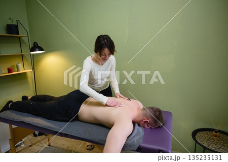 Female therapist performing back massage in wellness studio Female therapist performing back massage in wellness studio 135235131