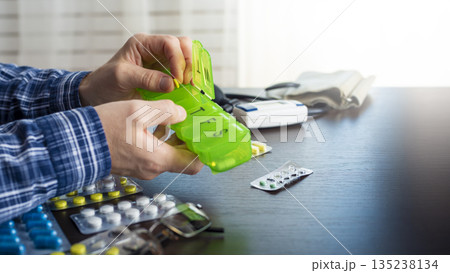 Middle aged caucasian man distributing scheduled dose of medication in dosette box 135238134