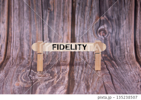Fidelity symbol. A wooden stick clasped by clothespins set over a beautiful Brown Grunge Wooden Texture Background. Business and Fidelity concept with copy space 135238507