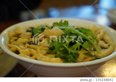 Delicious Korean style udon noodle soup with green vegetables in a white bowl, close up shot 135238641