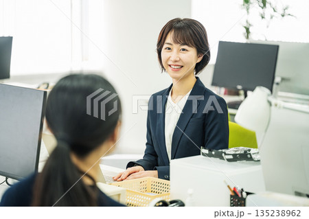 オフィスの机で同僚を話をする若い女性 オフィスの机で同僚を話をする若い女性 135238962