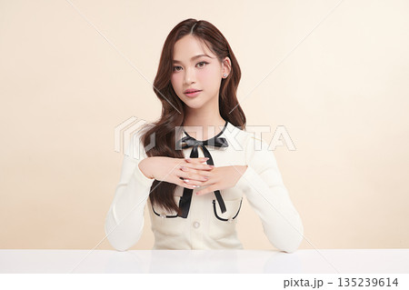 A beautiful young Asian woman with clean, fresh skin against a beige background. Skincare, facial treatment, cosmetology, beauty, and spa. An elegant portrait of an Asian woman. 135239614