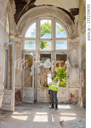 Inspector reviewing deteriorated mansion features with safety gear on site 135239650