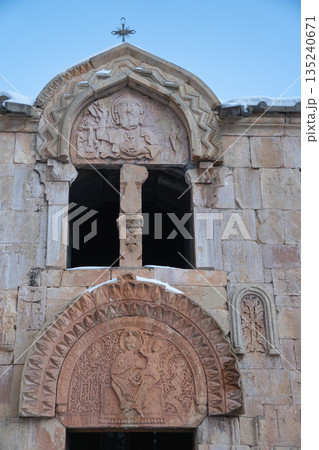Noravank Monastery facade with carved stone reliefs, arched window stands against sky, snow accents highlighting the historic Armenian architecture 135240671