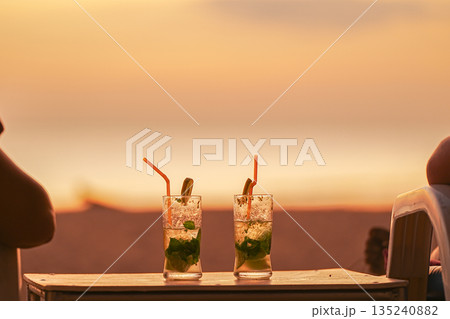 Two mojito cocktails served in glasses at sunset. A couple's vacation at resorts and entertainment, a honeymoon trip. Two people are watching the sunset sitting in sun beds and drinking cocktails 135240882