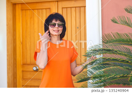 An adult woman in a short bright dress in the garden of her house near a palm tree 135240904