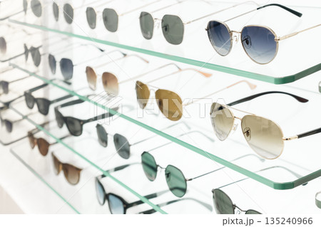 Various sunglasses are arranged neatly on glass shelves in a shop. The display shows multiple styles and colors of lenses. Bright light highlights the collection. High quality photo. Various sunglasses are arranged neatly on glass shelves in a shop. The display shows multiple styles and colors of lenses. Bright light highlights the collection. High quality photo. 135240966