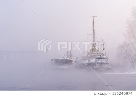 The outlines and silhouettes of old river ships moored to the shore in the winter fog. nostalgic art plot, historical heritage. High quality photo The outlines and silhouettes of old river ships moored to the shore in the winter fog. nostalgic art plot, historical heritage. High quality photo 135240974