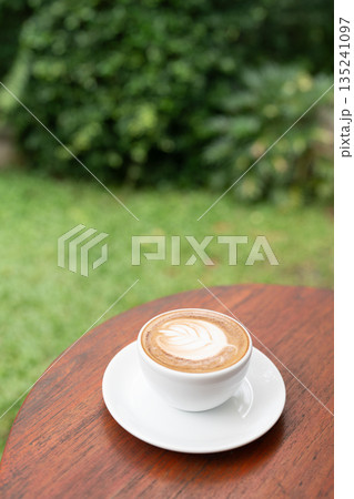 Cappuccino Coffee on a wooden round table, with lush green view Cappuccino Coffee on a wooden round table, with lush green view 135241097