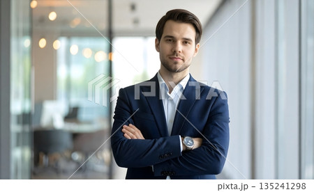 Confident business professional standing with arms crossed in a modern office environment with natural light conveying leadership, success and corporate professionalism 135241298