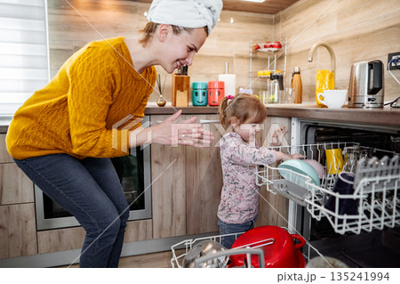 Little girl helping her mum load the dishwasher in the kitchen 135241994