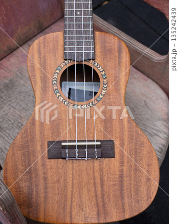 Close up of a wooden acoustic ukulele body. Vertical photo of a musical instrument with nylon strings and decorative rosette on a rustic background 135242439