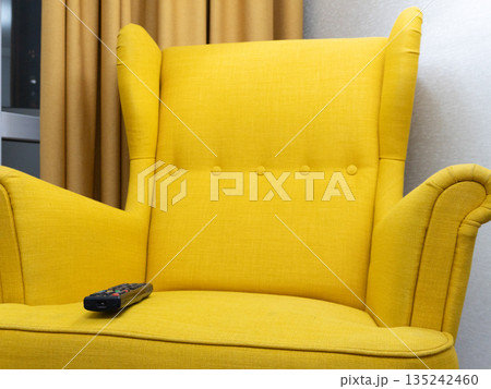 Yellow wingback armchair with a remote control on the seat. Comfortable furniture in a modern living room interior. Watching TV concept 135242460