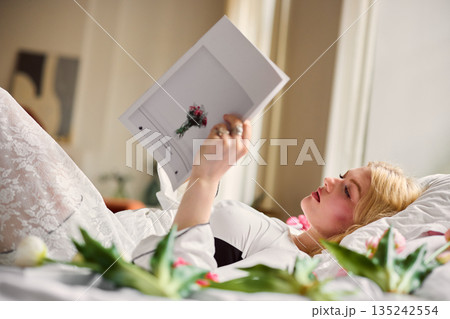 Woman reading magazine, Caucasian female relaxing in bed with tulips during tranquil afternoon rest Woman reading magazine, Caucasian female relaxing in bed with tulips during tranquil afternoon rest 135242554