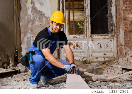 Man wearing helmet checks wooden beam within destroyed building structure Man wearing helmet checks wooden beam within destroyed building structure 135242561