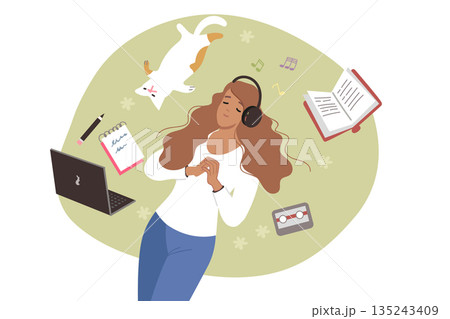 Woman listens to music on headphones, lies on lawn near cat and textbooks and takes break from work 135243409