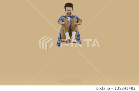 Happy, cheerful, funny, excited young man screaming while jumping up high on a trampoline 135243492