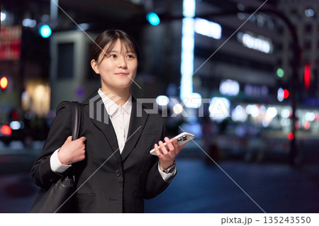 スマホを片手に夜の街に立つ若手ビジネスウーマン 135243550