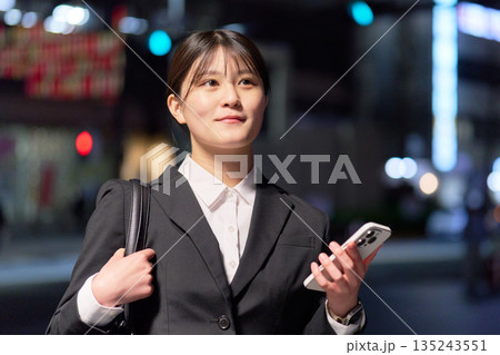 仕事帰りにスマホを片手に歩くスーツ姿の女性 仕事帰りにスマホを片手に歩くスーツ姿の女性 135243551