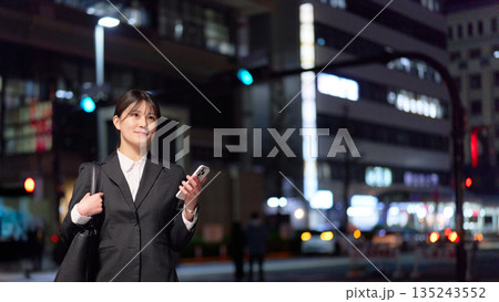 明るい表情で夜の街を歩く若手ビジネスウーマン 135243552