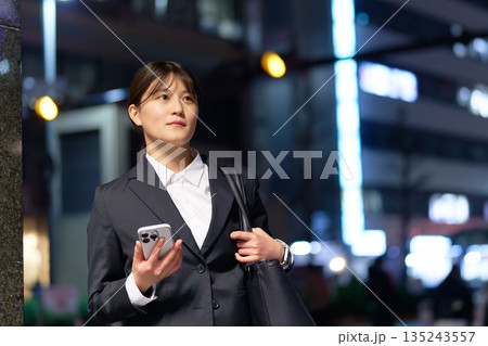 仕事帰りにスマホを片手に歩くスーツ姿の女性 仕事帰りにスマホを片手に歩くスーツ姿の女性 135243557
