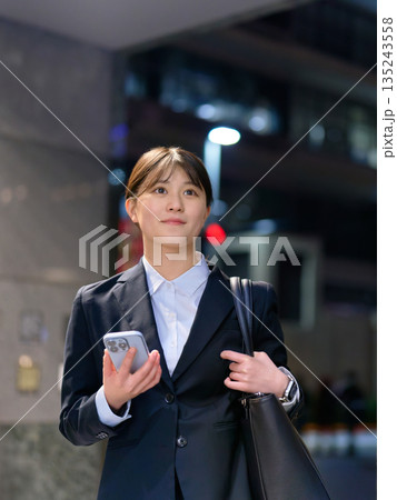 仕事帰りにスマホを片手に歩くスーツ姿の女性 135243558