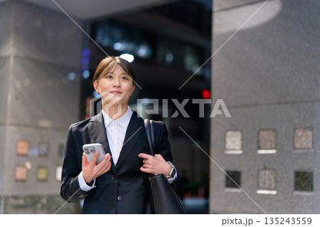 仕事帰りにスマホを片手に歩くスーツ姿の女性 135243559
