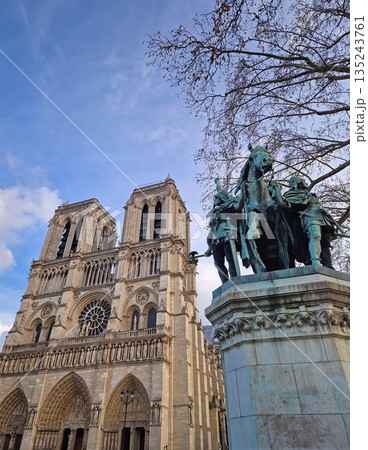Beautiful low-angle view of the Notre-Dame Cathedral in Paris. In the foreground, the bronze Charlemagne and His Guards statue stands prominently against the iconic twin towers Beautiful low-angle view of the Notre-Dame Cathedral in Paris. In the foreground, the bronze Charlemagne and His Guards statue stands prominently against the iconic twin towers 135243761