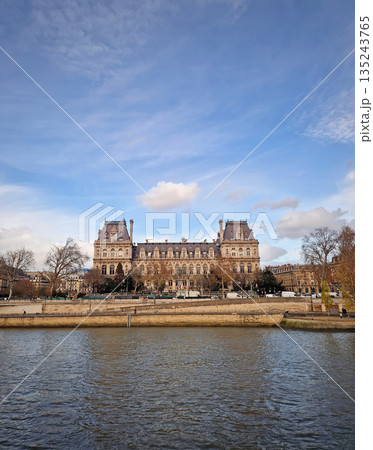 Beautiful view of the Hotel de Ville from the Seine riverside, showing the grand Neo-Renaissance facade and the riverbanks lined with trees and stone embankments 135243765