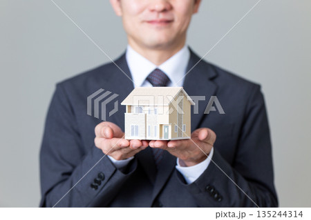 一戸建ての住宅模型を持つスーツ姿のミドル男性ビジネスマン 135244314
